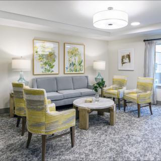 A cozy living room with a modern design featuring a sofa, four yellow chairs, a round coffee table, and decorative artwork on the walls.
