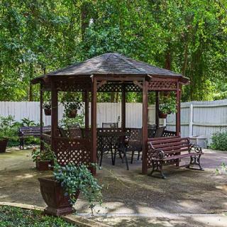A charming outdoor gazebo surrounded by greenery, featuring patio furniture and potted plants.