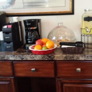 A cozy kitchen corner featuring a variety of fresh fruits on display, a coffee maker, and a beverage dispenser.