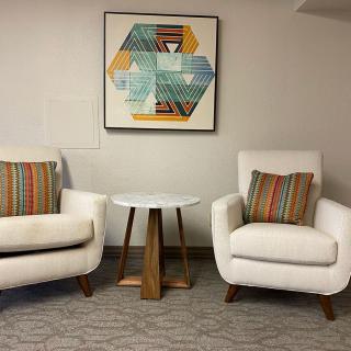 A modern sitting area with two white armchairs, a small wooden table, and geometric artwork on the wall.