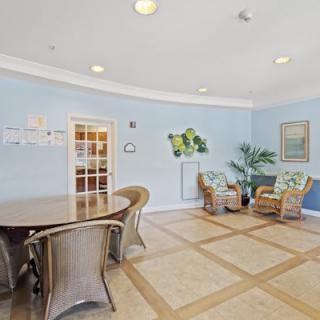 A cozy waiting area with wicker chairs, a large table, and decorative plants against light blue walls.