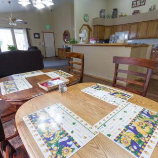 A cozy dining area with a wooden table and colorful placemats, adjacent to an open kitchen.