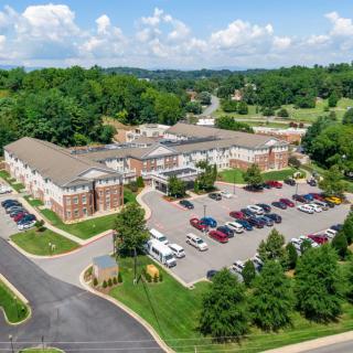Aerial view of a large building with a parking lot surrounded by trees and roads.