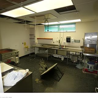 An abandoned commercial kitchen with signs of disrepair and a damaged ceiling.