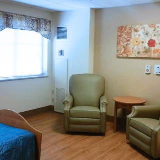 A cozy room interior with two chairs, a bed, and a small table near a window.