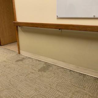 An office space with a stained carpet and a whiteboard on the wall.