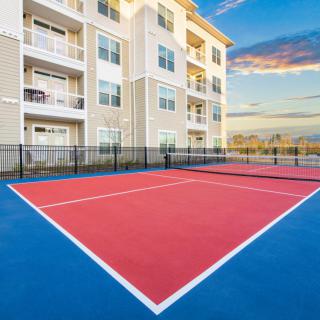A modern residential building with an outdoor tennis court at sunset.
