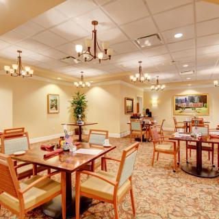 A well-lit dining area with neatly arranged tables and chairs, adorned with chandeliers and decorative wall art.
