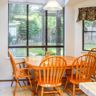 A cozy dining area with a wooden table and chairs, illuminated by natural light from large windows.