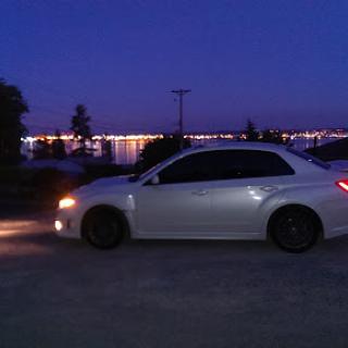 A sleek white car parked by the water under a twilight sky.