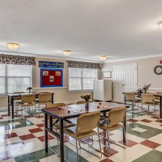 An empty classroom with desks and chairs arranged neatly, featuring bright windows and a patterned floor.