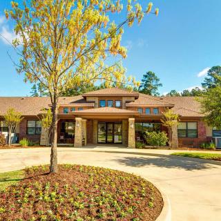 A modern building with a landscaped driveway and a large tree in front on a sunny day.