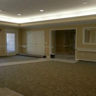 An empty room with carpeted flooring and several doors, illuminated by ceiling lights.