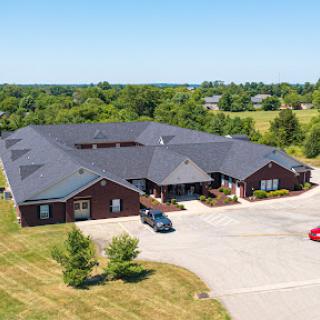 Aerial view of a residential building surrounded by lush greenery and a parking area.