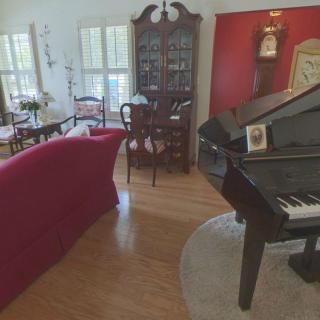 A cozy living room featuring a grand piano, red sofa, and elegant furniture pieces.