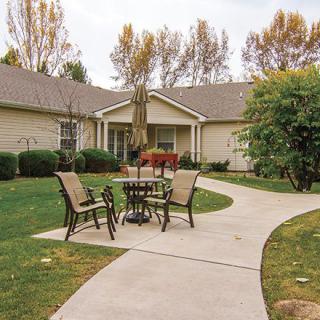 A serene outdoor patio with a table and chairs set on a paved walkway surrounded by greenery.