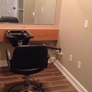 A small hair salon setup with a mirror, chair, and sink.