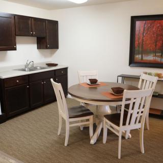 A minimalist kitchen and dining area featuring a round table with four chairs, dark cabinetry, and a framed artwork on the wall.