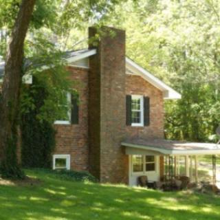 A brick house with a prominent chimney surrounded by trees and a lush green yard.