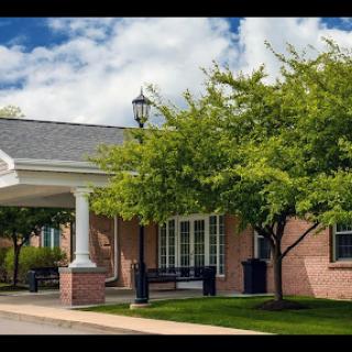 A welcoming entrance to a well-maintained building, surrounded by lush greenery and a clear blue sky.