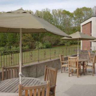 A serene outdoor patio with wooden tables and chairs, shaded by umbrellas, overlooking a lush garden.