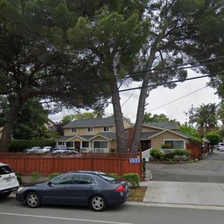A suburban street view featuring parked cars, houses, and large trees.