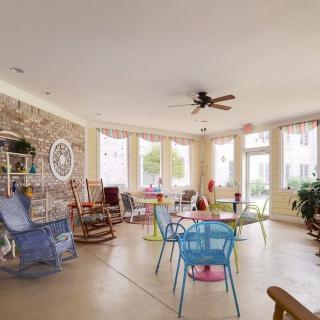 A bright and spacious living room with colorful chairs, rocking chairs, and large windows allowing ample natural light.