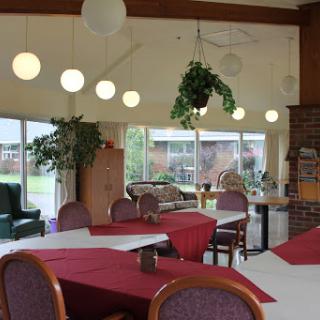 A cozy dining area featuring round tables with red tablecloths, modern lighting fixtures, and greenery.
