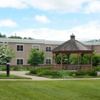 A serene outdoor setting with a gazebo in front of a building, surrounded by lush greenery and a well-kept lawn.