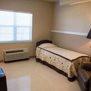 A minimalist bedroom with a single bed, chair, lamp, and window.