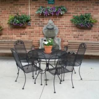A cozy outdoor patio area with metal chairs and a table, adorned with a potted plant and surrounded by hanging flowers.