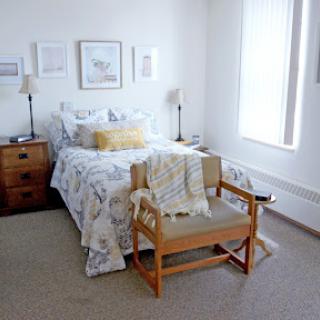 A cozy and well-decorated bedroom featuring a bed with floral bedding, a wooden chair, and soft natural light filtering through the window.