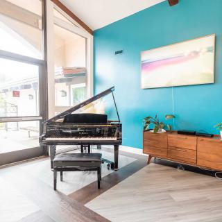 A stylish living room featuring a grand piano, turquoise accent wall, and mid-century modern furniture bathed in natural light.