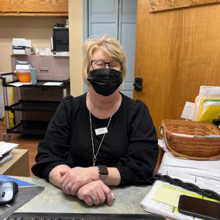 A receptionist wearing a mask at her desk in an office environment.