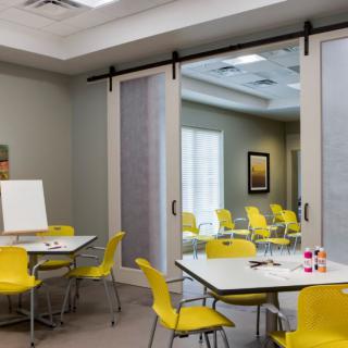 A modern meeting or classroom space with yellow chairs and sliding doors separating two rooms.