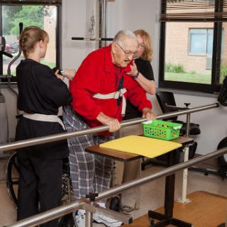 An elderly person receives assistance during a physical therapy session, supported by two caregivers.