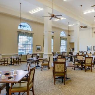 A spacious dining room with multiple tables and chairs, featuring high ceilings and large windows.