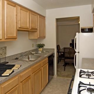 A cozy kitchen featuring wooden cabinets, a sleek countertop, and essential appliances including a gas stove and refrigerator, leading to a dining area.