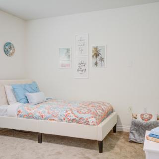 A minimalist bedroom featuring a neatly made bed with pastel bedding and simple wall decor.