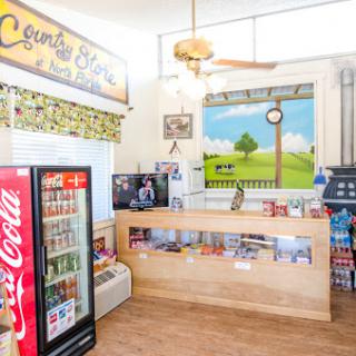 A cozy store counter featuring vending machines filled with snacks and beverages, complemented by cheerful wall art and a ceiling fan.