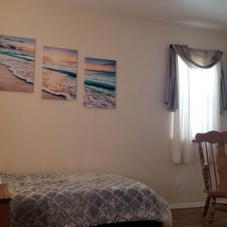 A cozy bedroom with ocean-themed artwork on the wall, a bed with patterned bedding, a window with curtains, and a wooden chair.