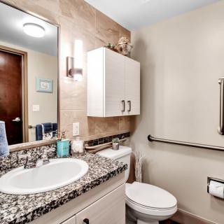 A modern bathroom featuring a granite countertop with a sink, a wall-mounted cabinet, and a toilet equipped with a handrail.