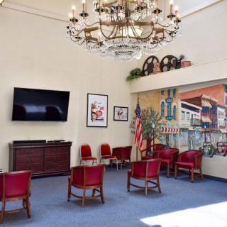 A spacious waiting area with red chairs, a mural on the wall, a large chandelier, and an American flag.