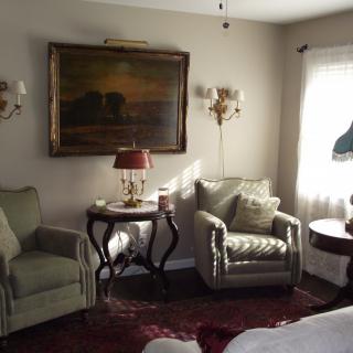 A cozy living room with elegant armchairs, a side table with a lamp, and a painting on the wall.