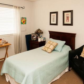 A cozy bedroom with a neatly made single bed, adorned with decorative pillows and artwork on the walls.
