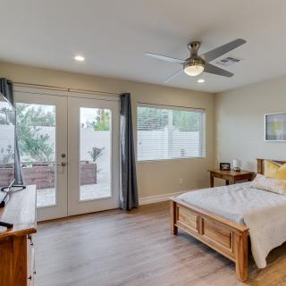 A modern bedroom with wooden flooring, a ceiling fan, and ample natural light from large windows and double doors.