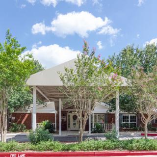 A building entrance surrounded by trees and landscaping under a partly cloudy sky.