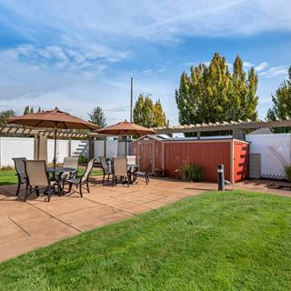 A sunny outdoor patio area with tables, chairs, and umbrellas set against a well-maintained lawn.