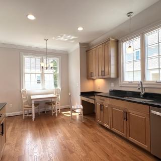 A modern kitchen with wooden cabinets, wood flooring, and a cozy dining area by large windows.