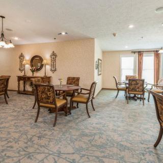 A well-decorated dining room with multiple tables and chairs, featuring elegant lighting and carpeted flooring.